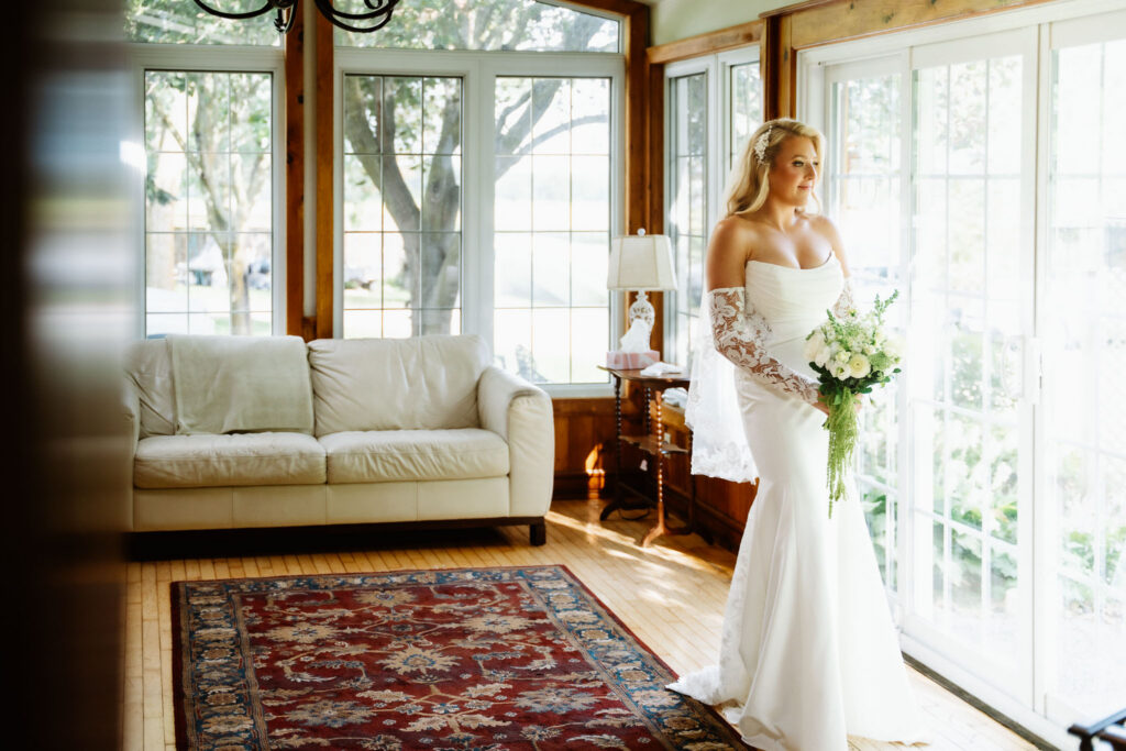 Ainsley holding her bouquet beside the big windows of a bright sunroom