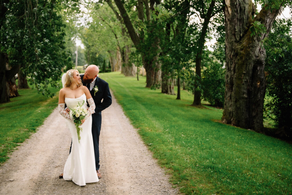 Ainsley and Rob sharing a quiet moment on a gravel lane lined with old trees during their Polmenna Barn wedding in Campbellford, Ontario