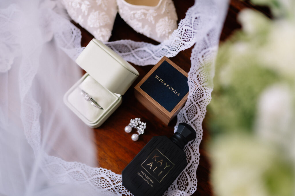 Wedding details flat lay with the ring box, pearl earrings, perfume bottle and lace veil edge