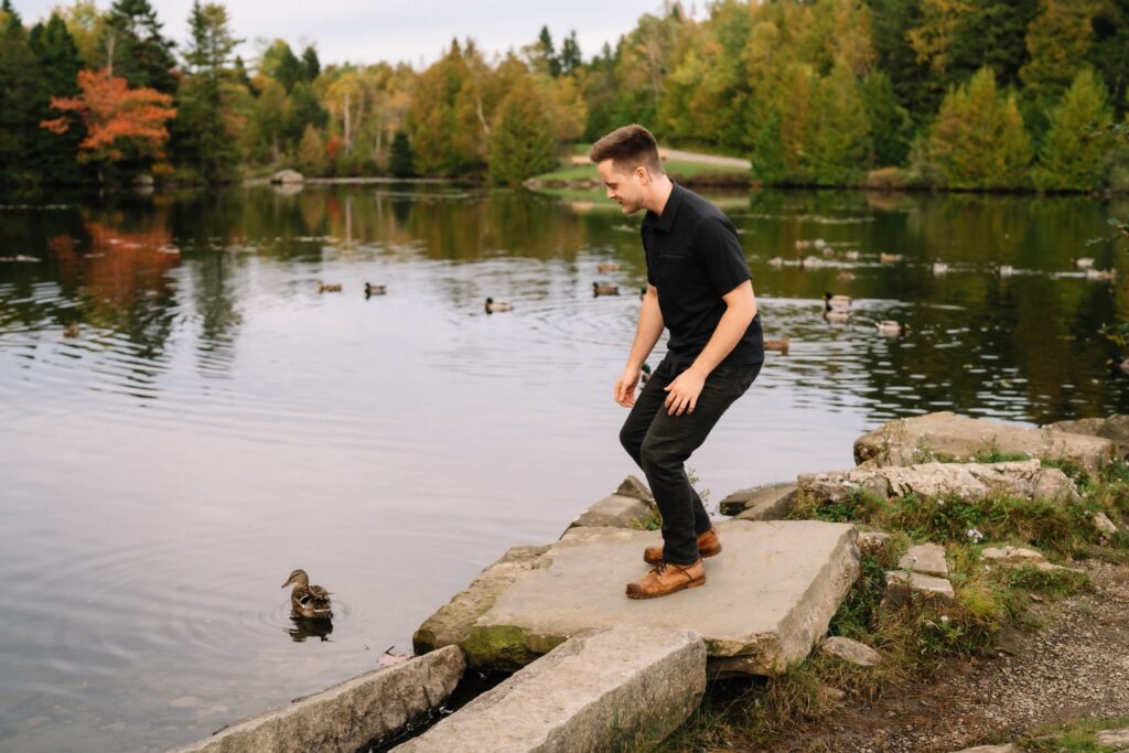 Alexandre balancing on a stone slab at the edge of the pond with a duck swimming nearby at Rockwood Park