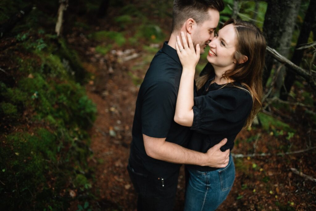 Briar smiling and holding Alexandre's face as they lean in for a kiss on a forest trail