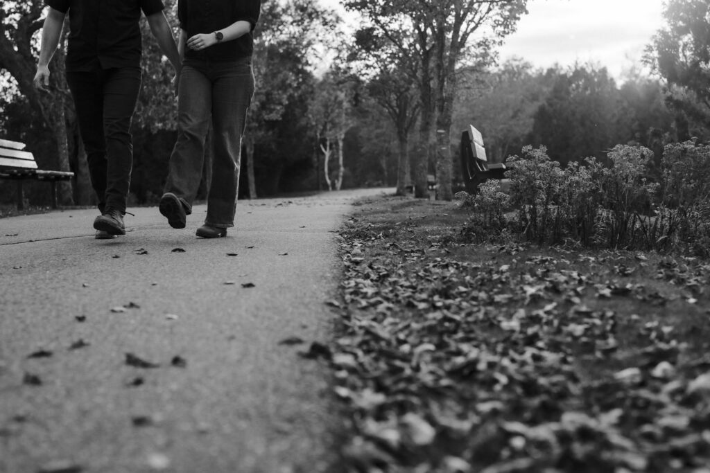 Black and white low-angle photo of Alexandre and Briar walking away along a path covered in fallen leaves