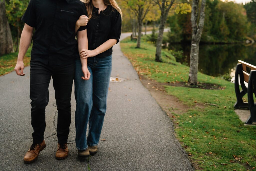 Alexandre and Briar walking arm in arm on a paved path beside the pond at Rockwood Park in fall